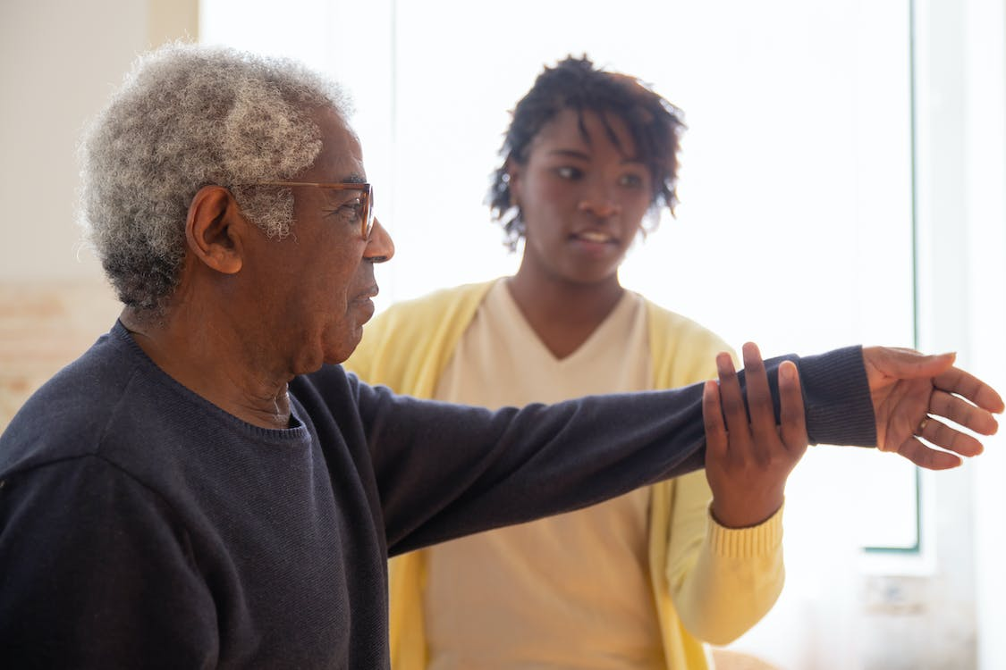 A caregiver is helping an elderly man to exercise.