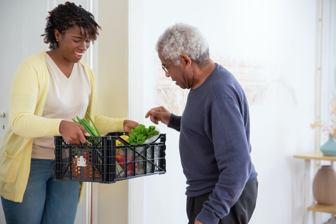 A caregiver is helping an elderly man with his groceries.