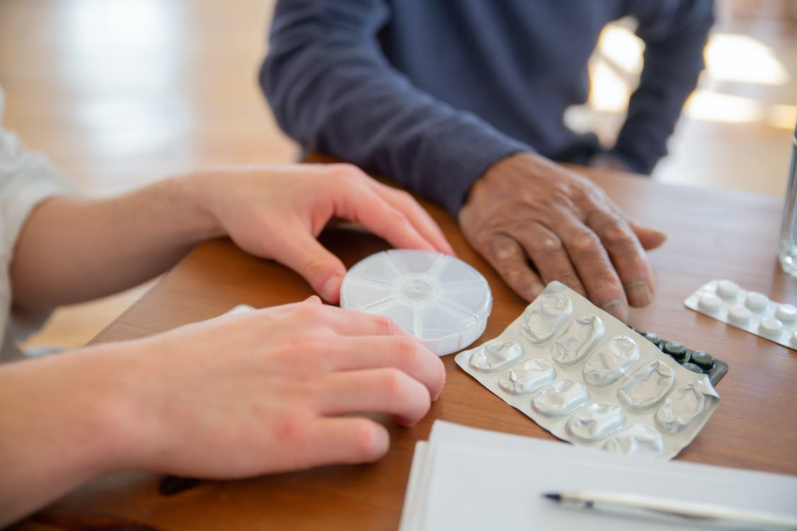 A caregiver is sorting the medicines for an elderly man.