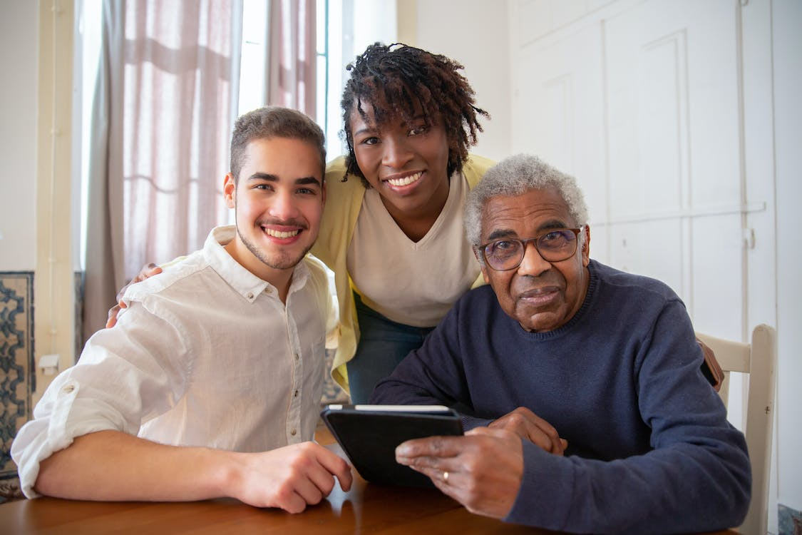 Two caretakers are posing with an elderly man, smiling for the camera.