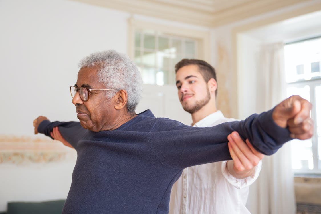 An elderly man is exercising with the help of a caregiver.