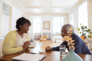 A senior citizen sitting at a desk with a young caregiver.