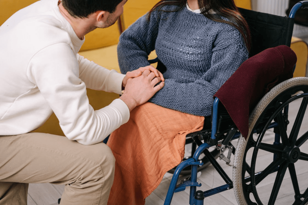 A caregiver is holding the hands of a woman sitting in a wheelchair.