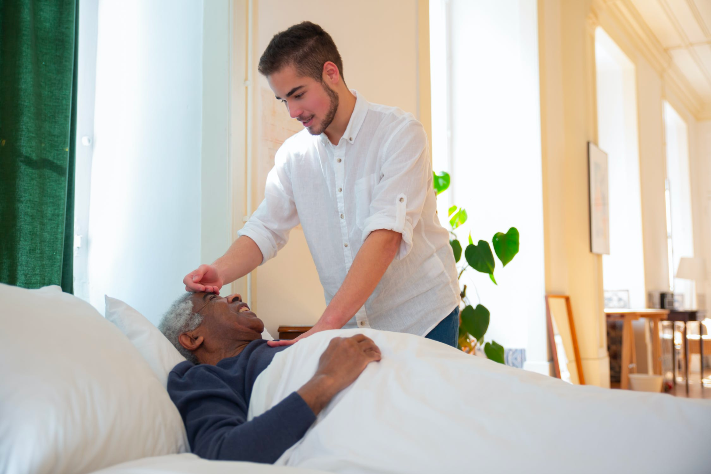 A caregiver looks after an elderly patient who lies in bed.