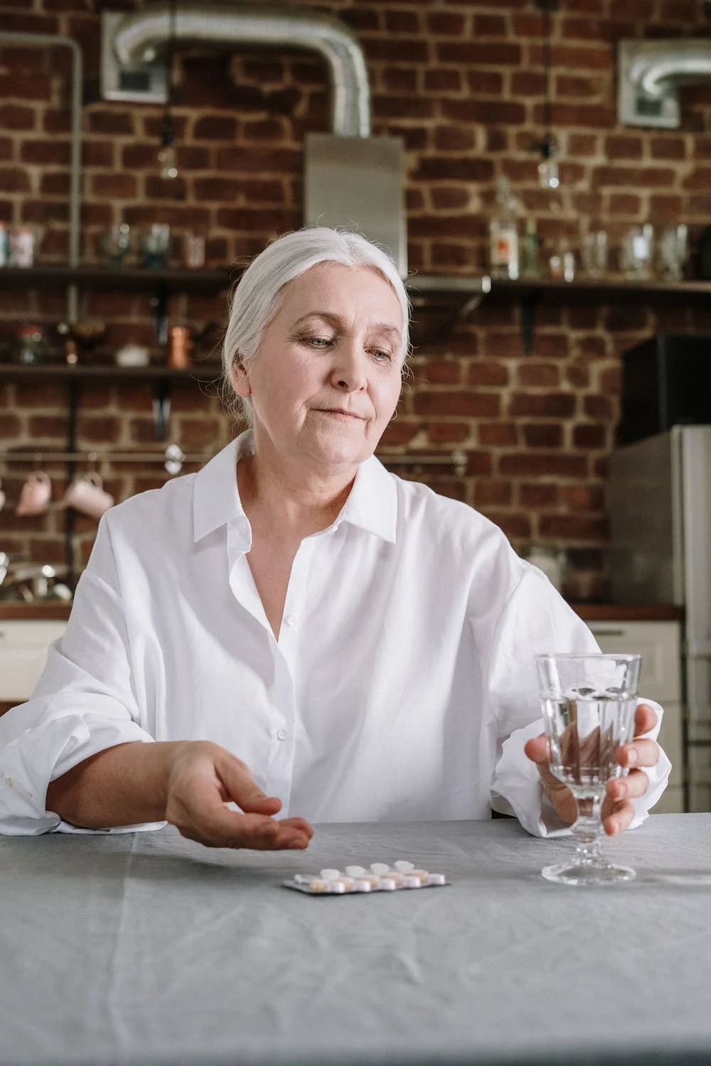  An independent older woman takes her medications while sitting at a table. 