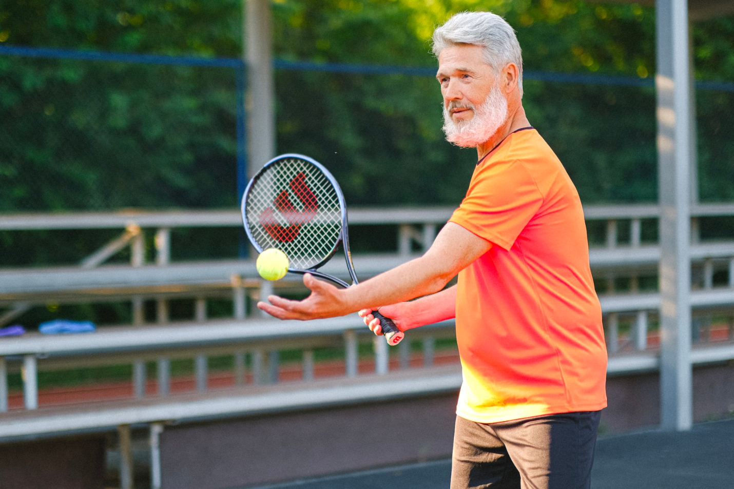  An older man exercises outdoors, playing tennis.